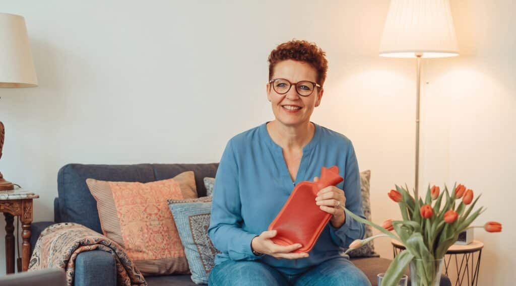 Silke Lemhöfer mit Wärmflasche auf dem Sofa – natürliche Hilfe bei Regelschmerzen