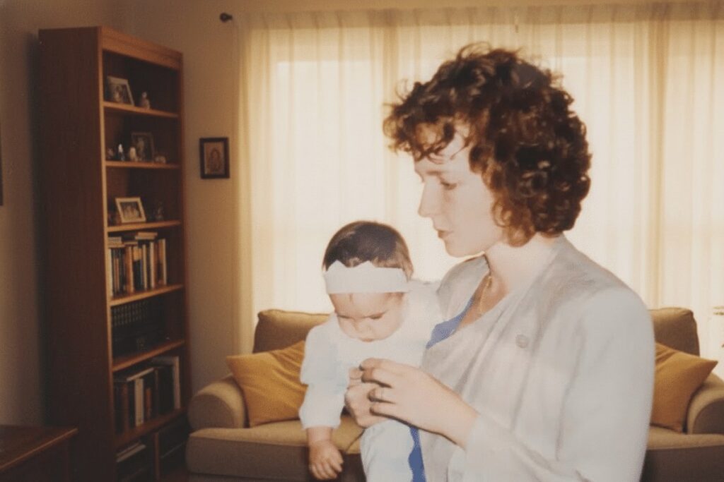 Junge Frau hält ihr Baby im Arm, warmes Wohnzimmerlicht